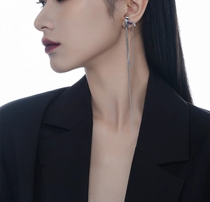 Detailed view of silver long chain tassel earring with purple stone on model ear