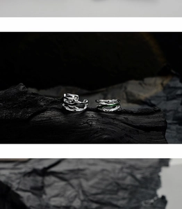 Macro detail of irregular silver earrings with green enamel on a dark textured background