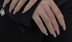 Close-up of long almond-shaped glossy nude brown press-on nails on hands with black suit