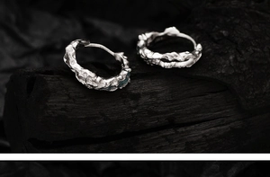 Macro detail of irregular lava texture on antique silver S925 earrings over dark wood