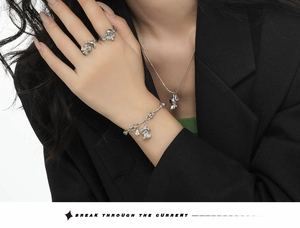 Detailed view of silver jewelry set including rings, necklace and charm bracelet on model