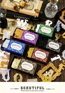 Detail of vintage gold foiled alphabet stickers in decorative boxes on wooden desk