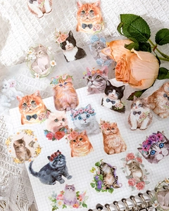 Close-up of decorative watercolor cat stickers on a grid journal with floral accents
