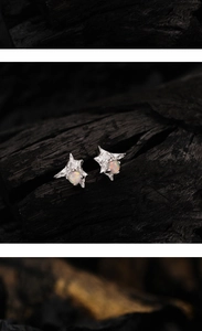 Macro detail of irregular star silver earrings featuring vibrant opal stones on black wood