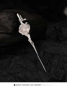 Nahaufnahme von Silber-Herzohrring mit Rosenquarz auf dunklem Kohlehintergrund