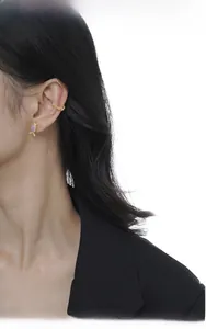 Close-up of a gold ear cuff and candy-shaped purple gemstone stud earring on a model