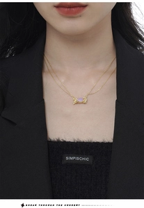 Close-up of a double-layered gold necklace with a purple candy-shaped pendant and pavé zircons