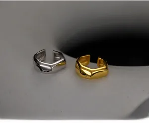 Détail des boucles d'oreilles géométriques argent et or sur un support en céramique chic