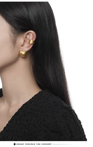 Macro detail of matte gold brushed ball earrings and cuff set on female model