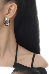 Close-up of oversized irregular liquid metal stud earrings in polished silver finish