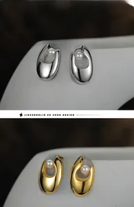 Detail von eleganten Gold- und Silberohrringen mit weißen Perlen und Hohlbogendesign auf Keramik