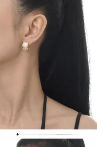Macro detail of C-shaped gold-plated hoop earrings with three rows of white zircon stones