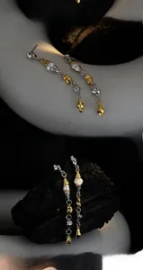 Close-up of asymmetrical gold and silver earrings with baroque pearls on dark stone
