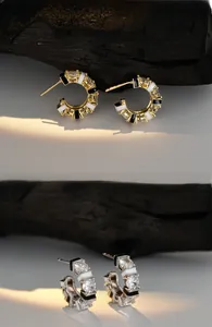 Detail of C-shaped earrings with zircons and black-white enamel on wood texture