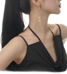 Close-up of elegant gold tassel earrings with freshwater pearls on a model wearing black