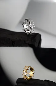 Detailed view of silver and gold star earrings with cubic zirconia on black wood
