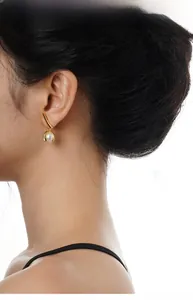 Detail of elegant gold leaf earrings with white pearl drop pendant worn by model