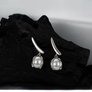 Detailed view of silver leaf pearl earrings on a textured black charcoal wood backdrop