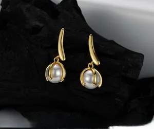 Detail of gold leaf earrings with round white pearls on a textured black rock background