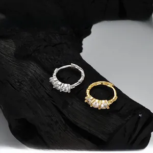 Macro detail of gold and silver textured earrings with three inlaid zircon stones