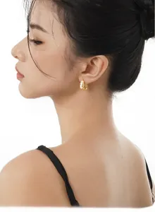 Gros plan de boucles d'oreilles créoles dorées à texture irrégulière avec incrustation
