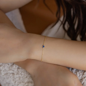Close-up of a gold chain bracelet with a rectangular blue gemstone on a woman's wrist
