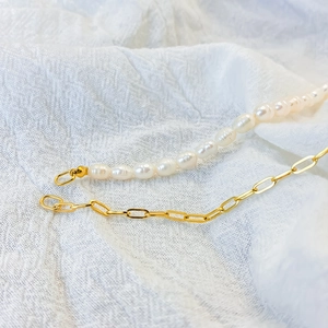 Detail of freshwater baroque pearl and gold plated chain link necklace on white fabric