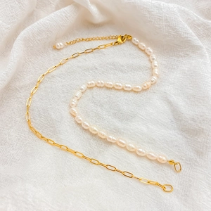 Macro view of gold chain and white freshwater pearl necklace on white linen background