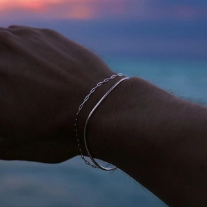 Close-up of stacked silver paperclip and snake chains worn by a model at the beach