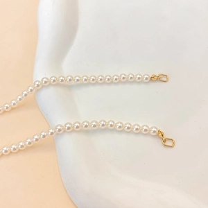 Gros plan de perles blanches avec fermoir mousqueton doré sur collier minimaliste