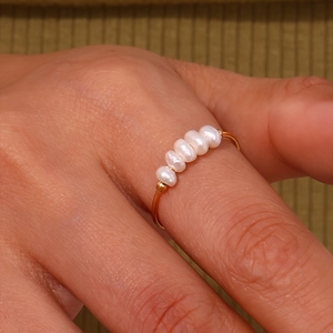 Macro detail of gold stainless steel ring featuring five natural freshwater pearls on model