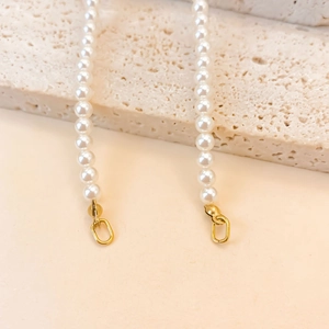 Détail d'une chaîne en perles brillantes avec fermoirs dorés sur fond de pierre naturelle