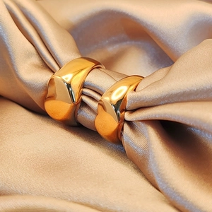 Close-up of chunky gold-plated hoop earrings on elegant champagne silk fabric background
