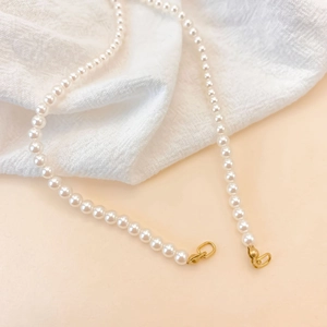 Élégant collier de perles blanches brillantes avec fermoirs dorés sur tissu texturé