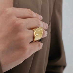 Detailaufnahme eines klobigen, goldfarbenen, unregelmäßigen Rings mit Spiegeleffekt
