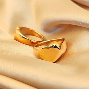 Detail of gold heart signet ring and minimalist band on champagne silk background
