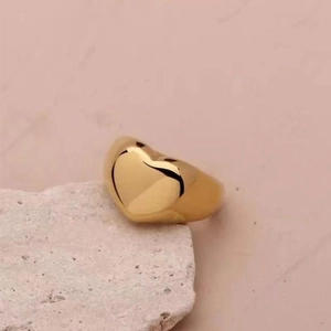 Detailed view of chunky gold heart ring on textured stone against pink background