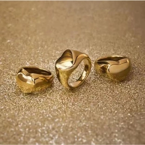 Detailed view of three polished gold liquid heart rings on shimmering golden sand