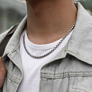 Gros plan d'un collier chaîne box argenté porté sur un t-shirt blanc et veste en jean