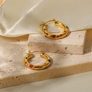 Detailaufnahme goldener Creolen mit bunten Kristallen auf weichem Seidenstoff