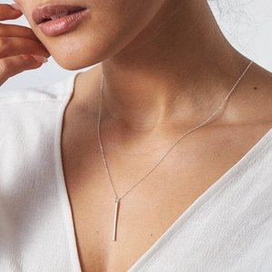 Close-up of a minimalist silver vertical bar pendant necklace worn by a female model