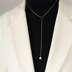 Detail of a gold Y-shaped necklace with a white pearl pendant on a black sweater