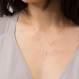 Detailed view of a minimalist golden vertical bar pendant necklace on a female model