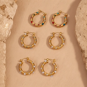 Detailansicht von drei goldenen Creolen mit bunten Zirkonia und Perlen auf Sand