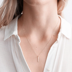 Close-up of a minimalist rose gold vertical bar pendant necklace worn by a model