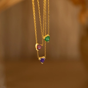 Trois colliers dorés avec pendentifs cœurs en rubis, émeraude et améthyste de naissance