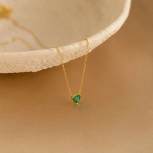 Détail d'un pendentif en pierre précieuse vert émeraude en forme de cœur sur chaîne dorée