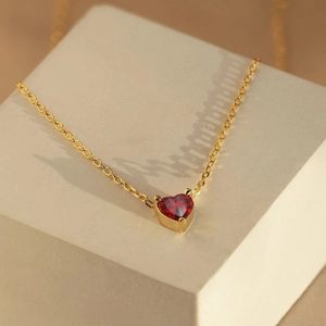 Gros plan d'un collier en acier doré avec pendentif cœur en zircon rouge brillant