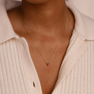 Élégant collier doré avec pendentif en pierre précieuse rouge porté par un mannequin