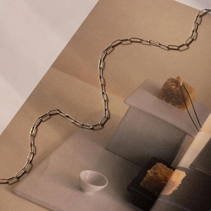 Detailed close-up of a silver paperclip chain necklace on a minimalist lifestyle magazine